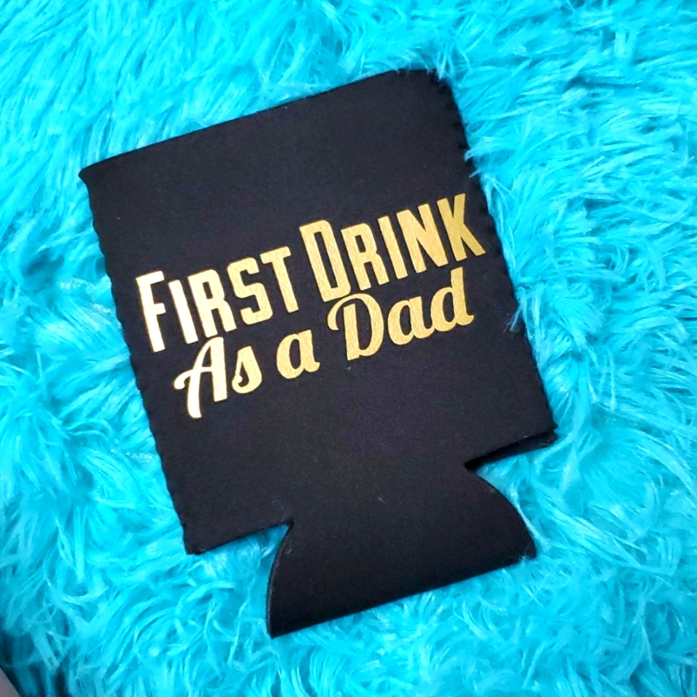 "First drink as a dad" gold and black beer cozy.